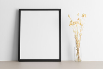Black frame mockup with a lagurus decoration on the beige table.