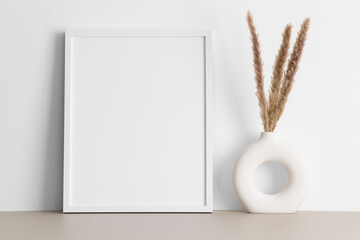 White frame mockup with a pampas decoration on the beige table.