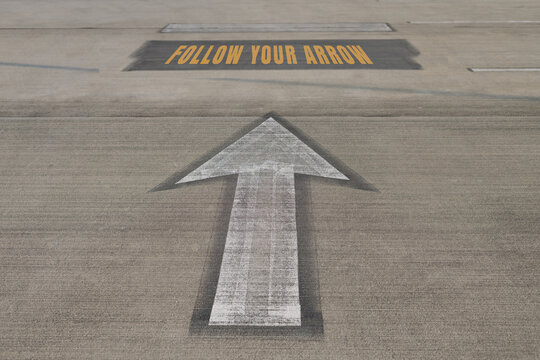 FOLLOW YOUR ARROW, written on an asphalt road above the arrow painted on road.