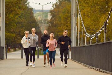 Team of sporty people men and women running together along a bridge having sport workout outdoors....