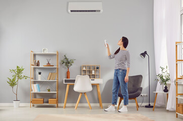 Tenant or apartment owner switches modern air conditioning system at home. Young woman standing in...