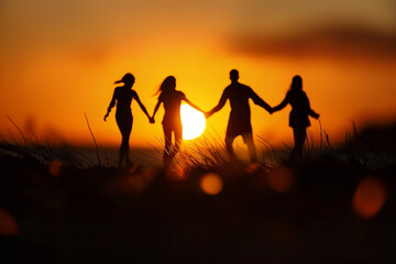 Silhouette of four people holding hands at sunset.