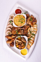 Top view Assorted roasted meats, colorful vegetables, and golden potatoes garnished with fresh parsley and savory sauces on a white platter