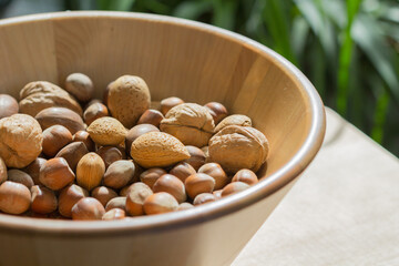 Assorted various nuts in a big wooden bowl against a leafy green background. Macro photography - 776259604