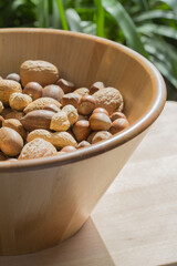 Assorted various nuts in a big wooden bowl against a leafy green background. Macro photography - 776259837