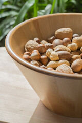 Assorted various nuts in a big wooden bowl against a leafy green background. Macro photography - 776260001