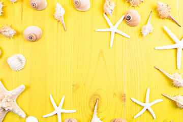 Composition seen from above with yellow wooden background and shells, conchs and starfish on the margins and with copy space in the center. Summer concept - obrazy, fototapety, plakaty