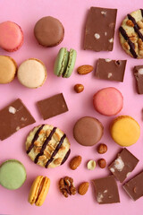 Pastel macarons, almond chocolate, peanut butter cookies and various nuts on bright pink background. Top view.