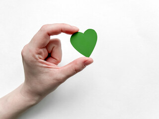 Female hand holding a green paper heart on a white background, Earth Day, April 22.