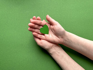 Female hands hold a green paper heart on a green background, Earth Day, April 22