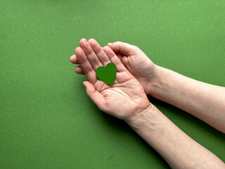 Female hands hold a green paper heart on a green background, Earth Day, April 22