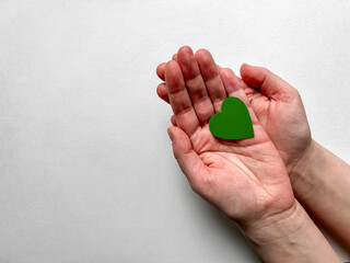 Female hands holding a green paper heart on a white background, Earth Day, April 22.