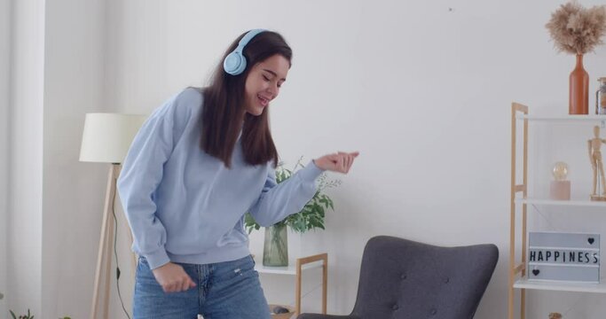 In joyful home, happy woman, immersed in happiness, dances while listening to music using headphones. The scene captures the essence of relaxation, fun, and the joy of letting loose in the comfort.
