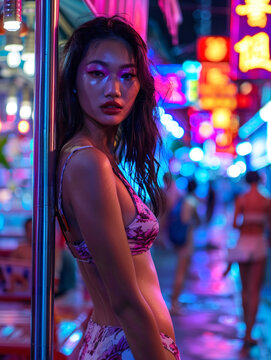 Beautiful sexy asian girl woman tanned skin looking at the camera standing next to a metal pole at night in a busy street nightlife party