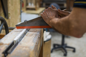 Older man's hands cutting with saw on antique workbench