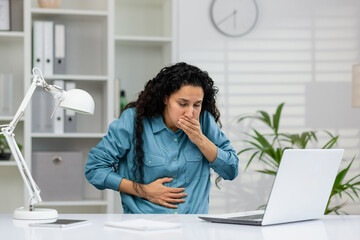 An adult woman experiencing nausea at her desk with a hand over her mouth and holding her stomach,...