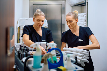Two maids restocking housekeeping trolley while working in hotel.
