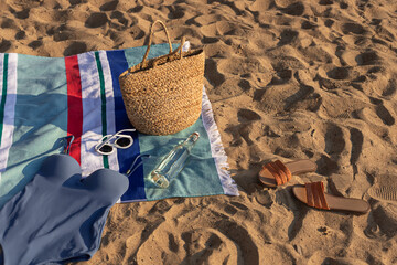 Jute beach bag and swimsuit on the striped towel and flip flops on the sand. Summer vacation lifestyle concept