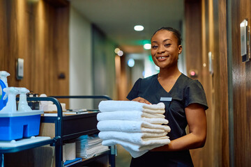Happy black hotel man with stack of clean towels looking at camera.