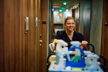 Happy maid pushing room attendants' trolley while cleaning guest rooms in  hotel.