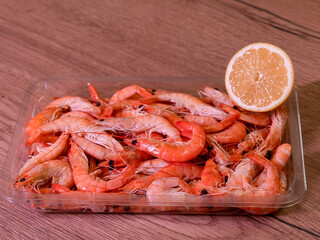 unpeeled shrimp in plastic with lemon, photo from the side, wood background
