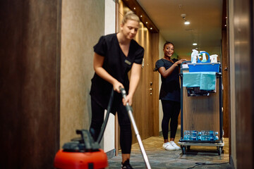 Young black maid and her female co-worker cleaning hotel hallway.