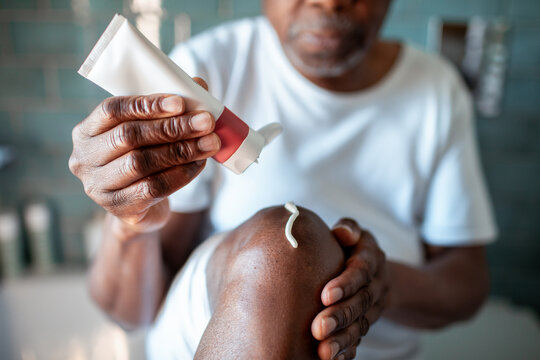 Senior Black man applying cream on knee at home