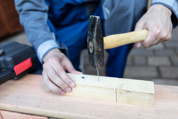 Close up of hands of carpenter holding hammer and knocking in nail the wood	