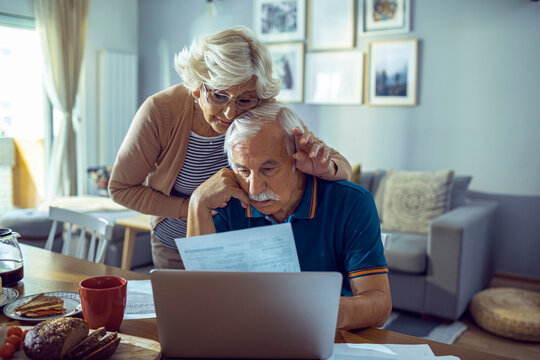Senior couple reviewing documents and using laptop at home