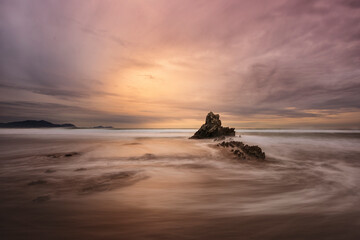 Sunset on Atxabiribil beach in Sopelana, Bizkaia with a rock emerging from the water and a dramatic...