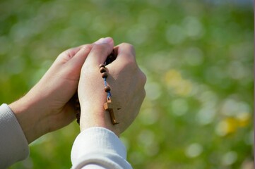 Man praying rosary with folded hands in peaceful green nature