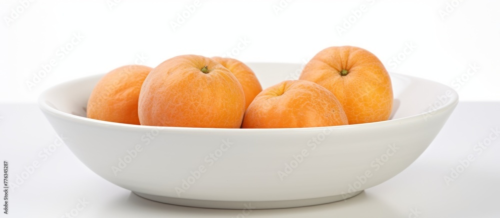 Poster arranged on a wooden table is a white bowl containing four ripe oranges, creating a simple and refre