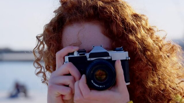 Portrait of young redhead woman taking a photo with a vintage camera. Teenager looking at camera.