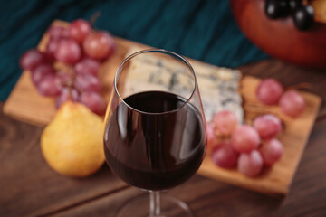 Glass of rich red wine served with cheese plate and fruits on dark wooden background. Appetizers...