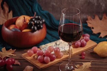 Glass of red wine served with blue cheese on dark wooden background. Autumn picnic with wine and cheese platter, fruits and dry leaves in rustic style