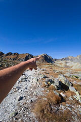 Man hand is pointing at the top and peak of the mountain. Tourist, hiker and mountaineer is showing destination. Landscape in autumn and fall, sunny day with blue sky. Shallow focus and copy space.