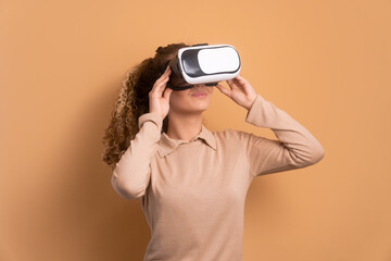 cheerful teen girl Using VR headset and gesturing in beige studio background. virtual reality,...