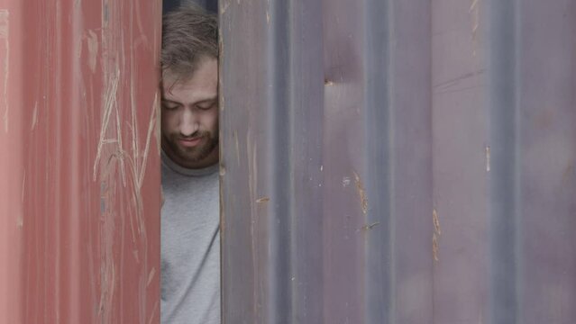 Disappointed man peeking through opening in shipping containers - medium shot