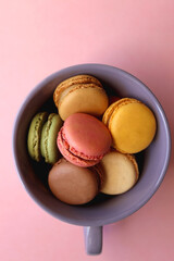 Purple cup filled with pastel macarons on pink background. Top view.