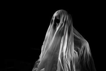 Eerie ghost figure shrouded in a white veil against a dark background. - obrazy, fototapety, plakaty