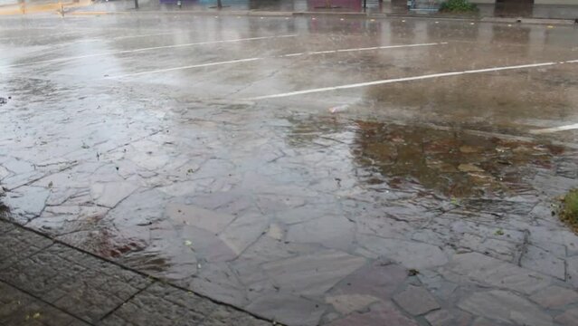 Aguacero con tormenta en la ciudad. La lluvia cae sobre la acera con viento de furia sobre la calle asfaltada,  produce r&aacute;fagas de agua. Corre por el cord&oacute;n del asfalto arrastrando basura pl&aacute;stica.