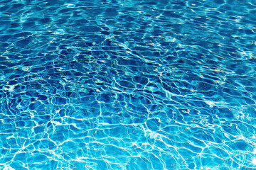 Close-up of a swimming pool filled with clear blue water. Sunlight dances on the surface, creating ripples and sparkling reflections