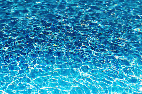 Close-up of a swimming pool filled with clear blue water. Sunlight dances on the surface, creating ripples and sparkling reflections