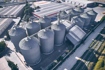 Agricultural facilities for grain storage and processing. Silver colored granaries at steep rural area. Silos storage tanks aerial view