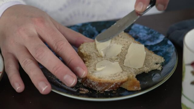 Close-up hand spreading butter on slide of bread for breakfast nutrition. Knife spreads buter on carb food
