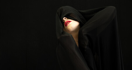red made up mouth of female beauty model portrait covered with black fabric on black background, wide banner portrait