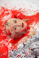 Portrait of young naked sexy blond woman in red, white and black color painted, lies decorative sensual seductive on the colorful studio floor in abstract expressive bodypainting art