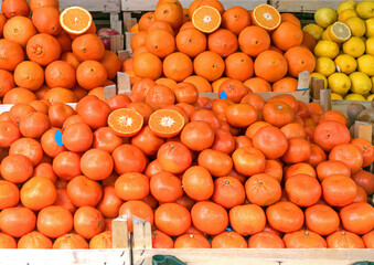 Large pile of oranges lemons and other citrus fruits in wooden crates on market stall
