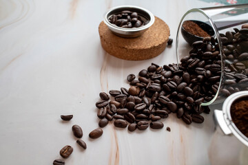 Roasted aromatic coffee beans are scattered from a jar on light marble table. Close-up, selective...