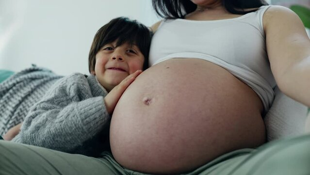 Happy small 5 year old boy gently rubs mother's pregnant belly during late stage of pregnancy. Happiness maternal concept between loving genuine family moment